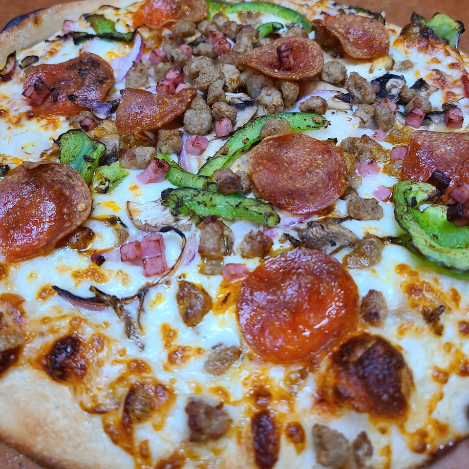 Close-up of a Pizza King pizza with pepperoni, sausage, ham, green peppers, onions, and mushrooms.