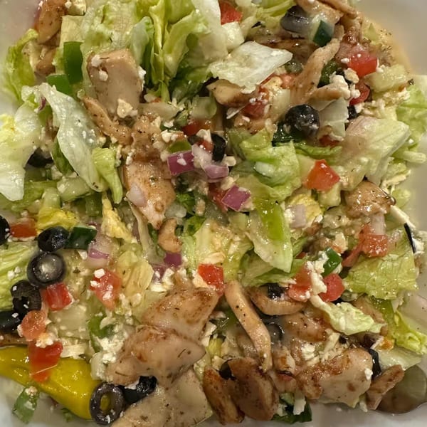 Close-up of a fresh salad with grilled chicken, lettuce, tomatoes, olives, and feta cheese.