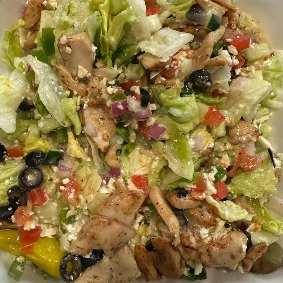 Close-up of a fresh salad with grilled chicken, lettuce, tomatoes, olives, and feta cheese.