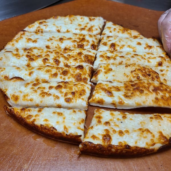 Freshly baked Pizza King cheesy breadsticks, cut into strips, on a brown cutting board.