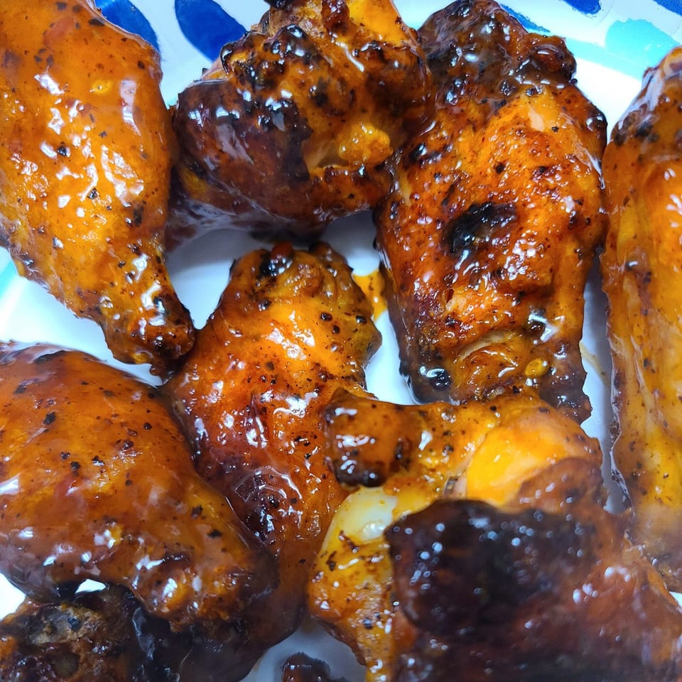 Close-up of several glossy, sauced chicken wings with visible char marks on a white plate.